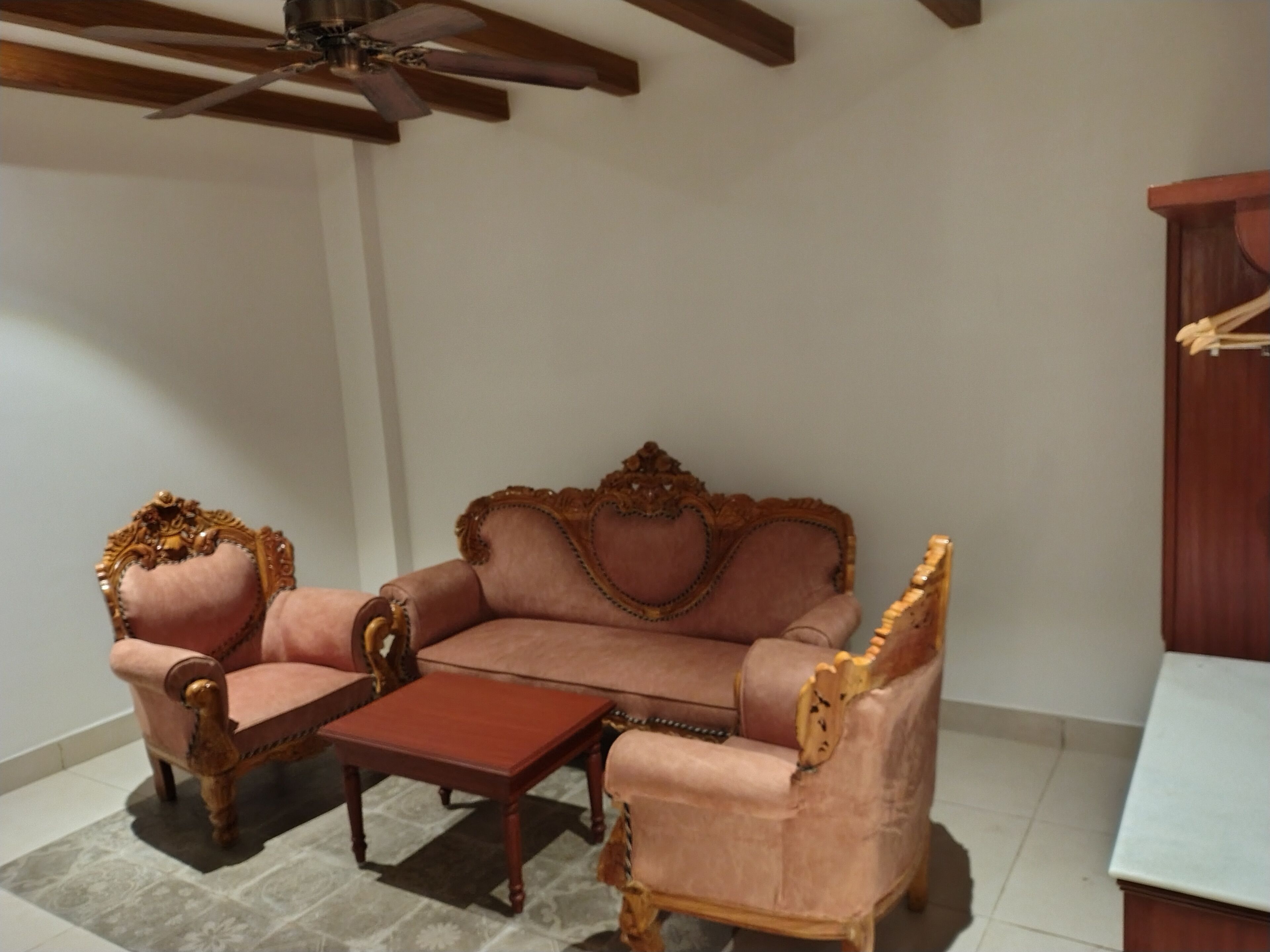 A room with a wooden ceiling fan, a pink sofa set, a wooden coffee table, and a wooden cabinet.