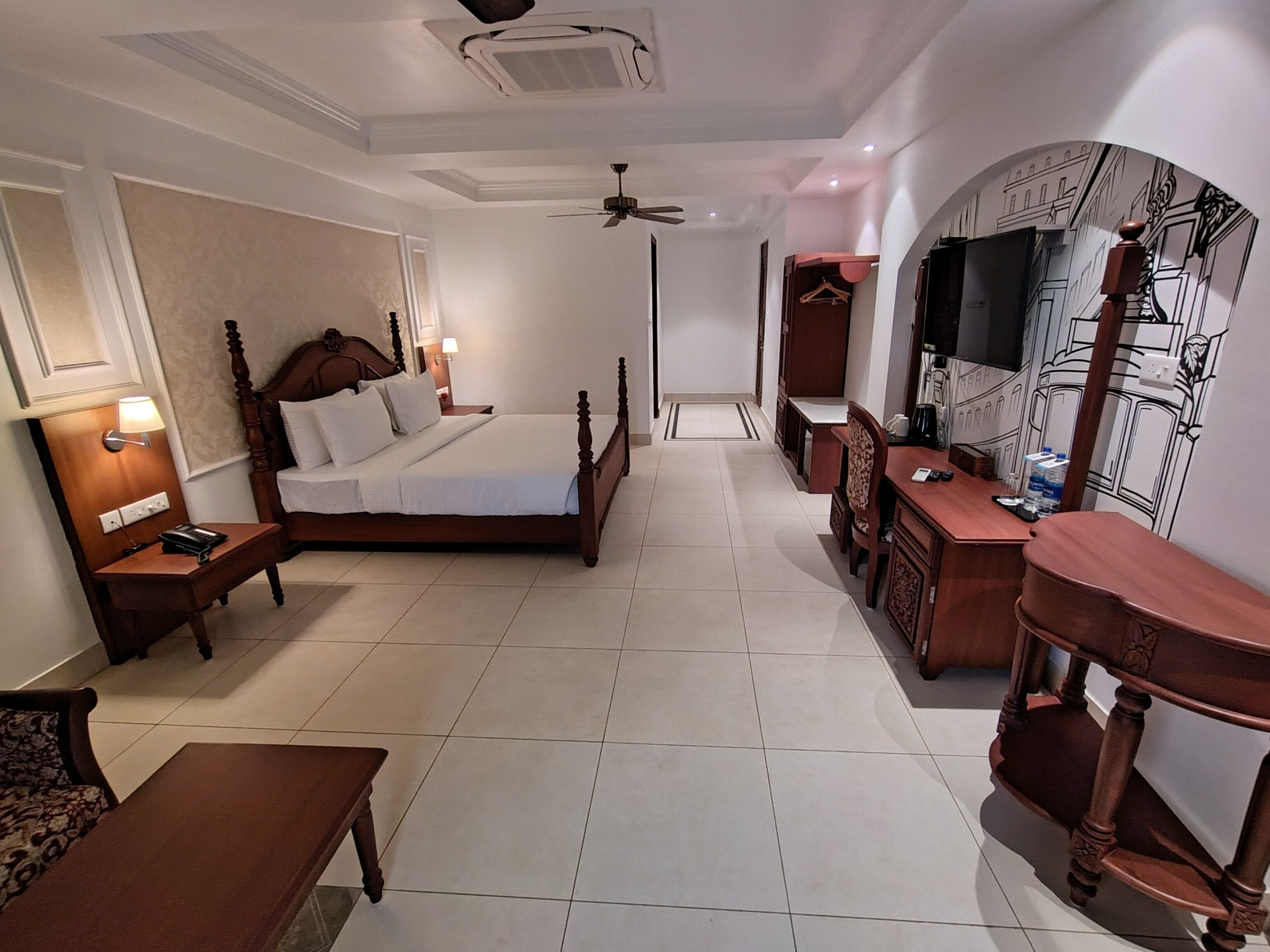 A hotel room with a bed, bedside tables, a desk, a chair, a TV, and a wardrobe.