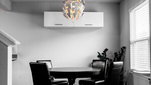 Un coin repas avec une table ronde, quatre chaises, un lustre moderne et un appareil de climatisation blanc placé au-dessus.