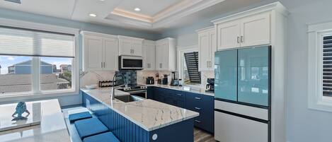 A modern kitchen with a marble island, built-in appliances, and a large window overlooking a residential area.
