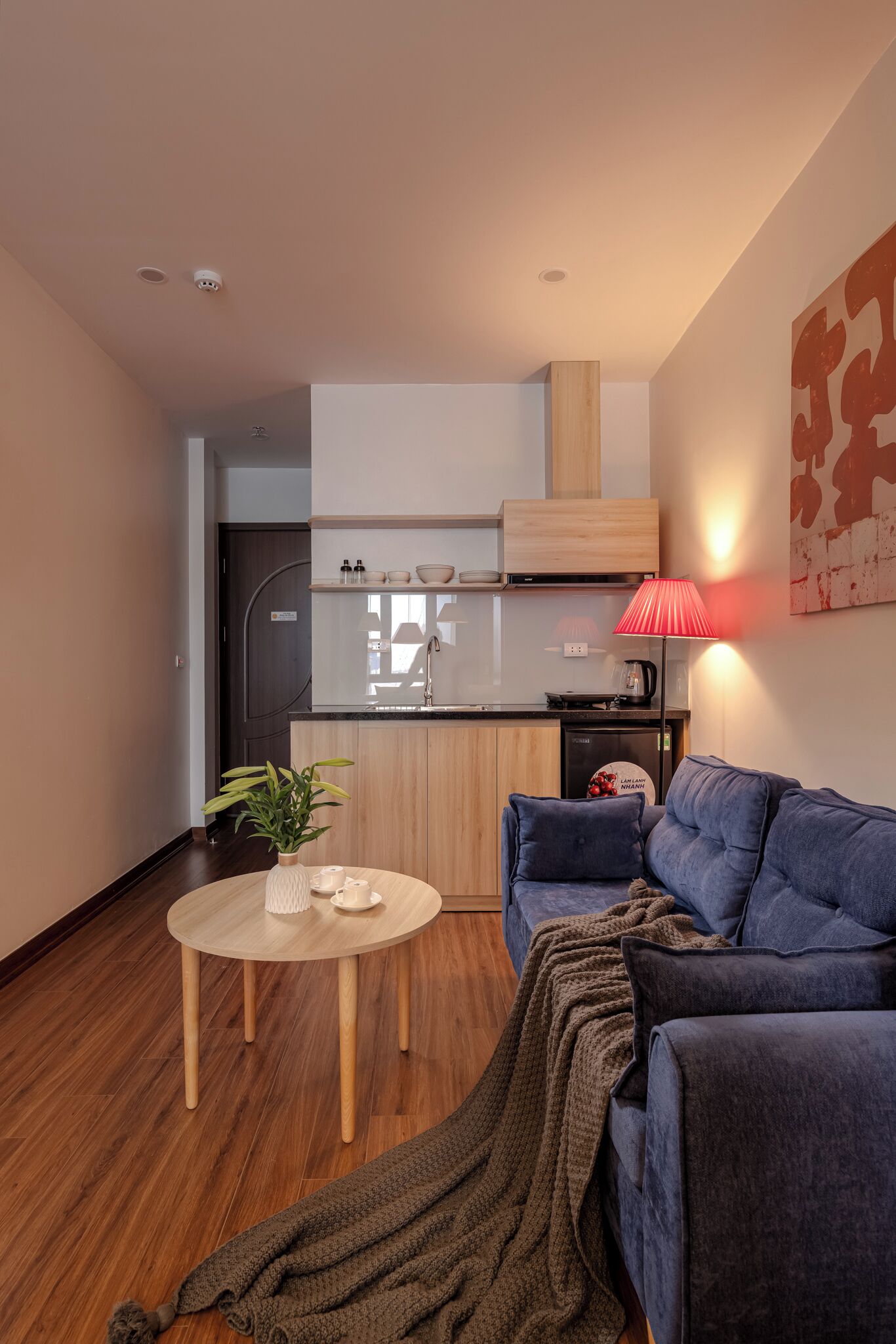 A modern living room with a blue sofa, a round wooden coffee table, and a kitchen area in the background.