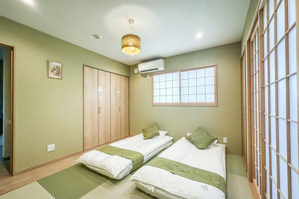 A room with two beds, a window, a wardrobe, and an air conditioning unit.