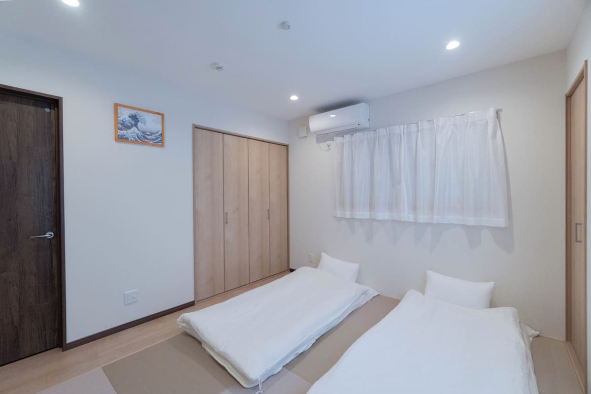 A bedroom with two single beds, a wooden wardrobe, a wall-mounted air conditioner, and a framed picture.