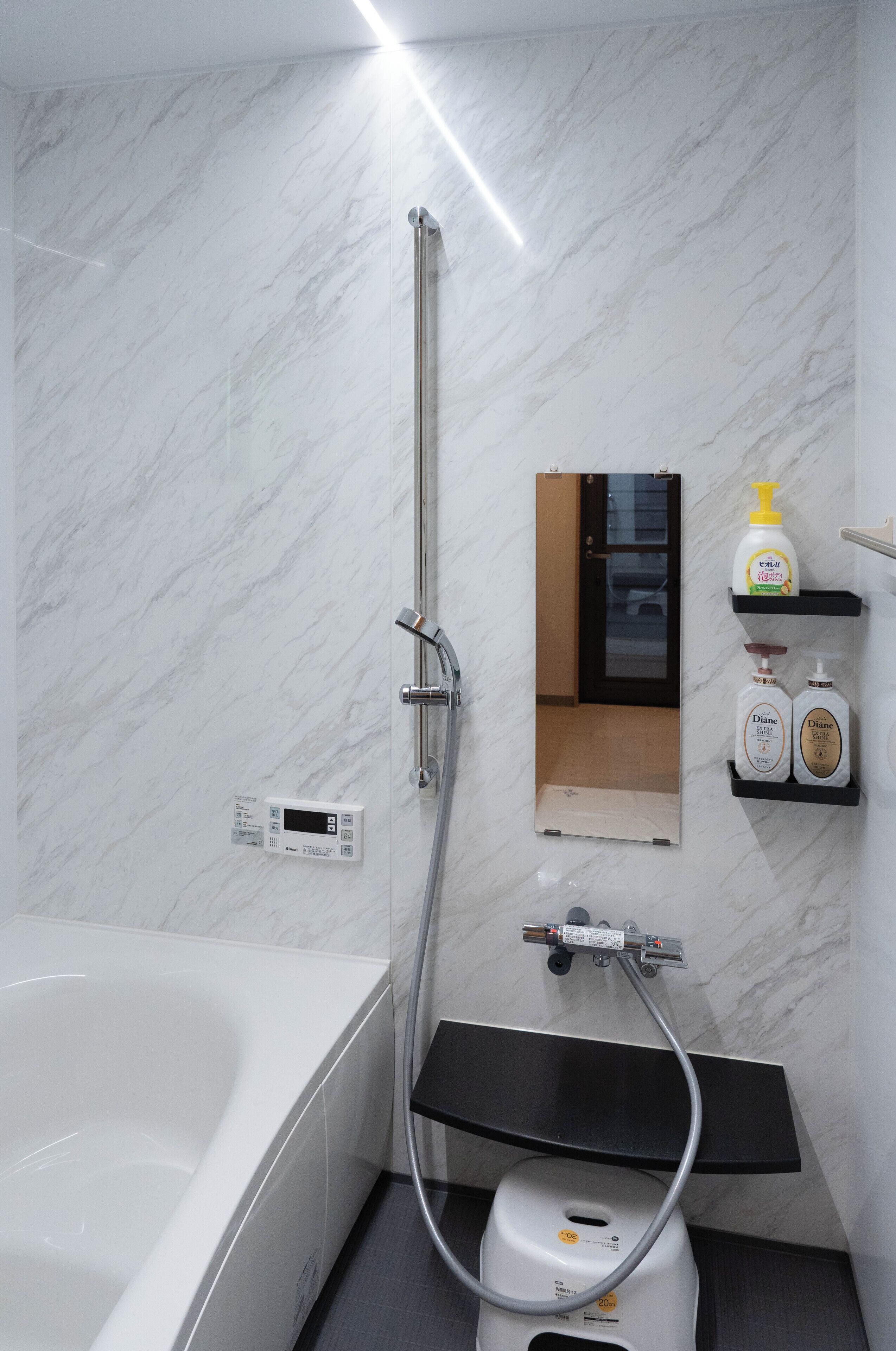 Un bagno moderno con una parete in marmo bianco, una vasca freestanding, un soffione doccia a mano, un portasciugamani e due flaconi di bagnoschiuma Diane.