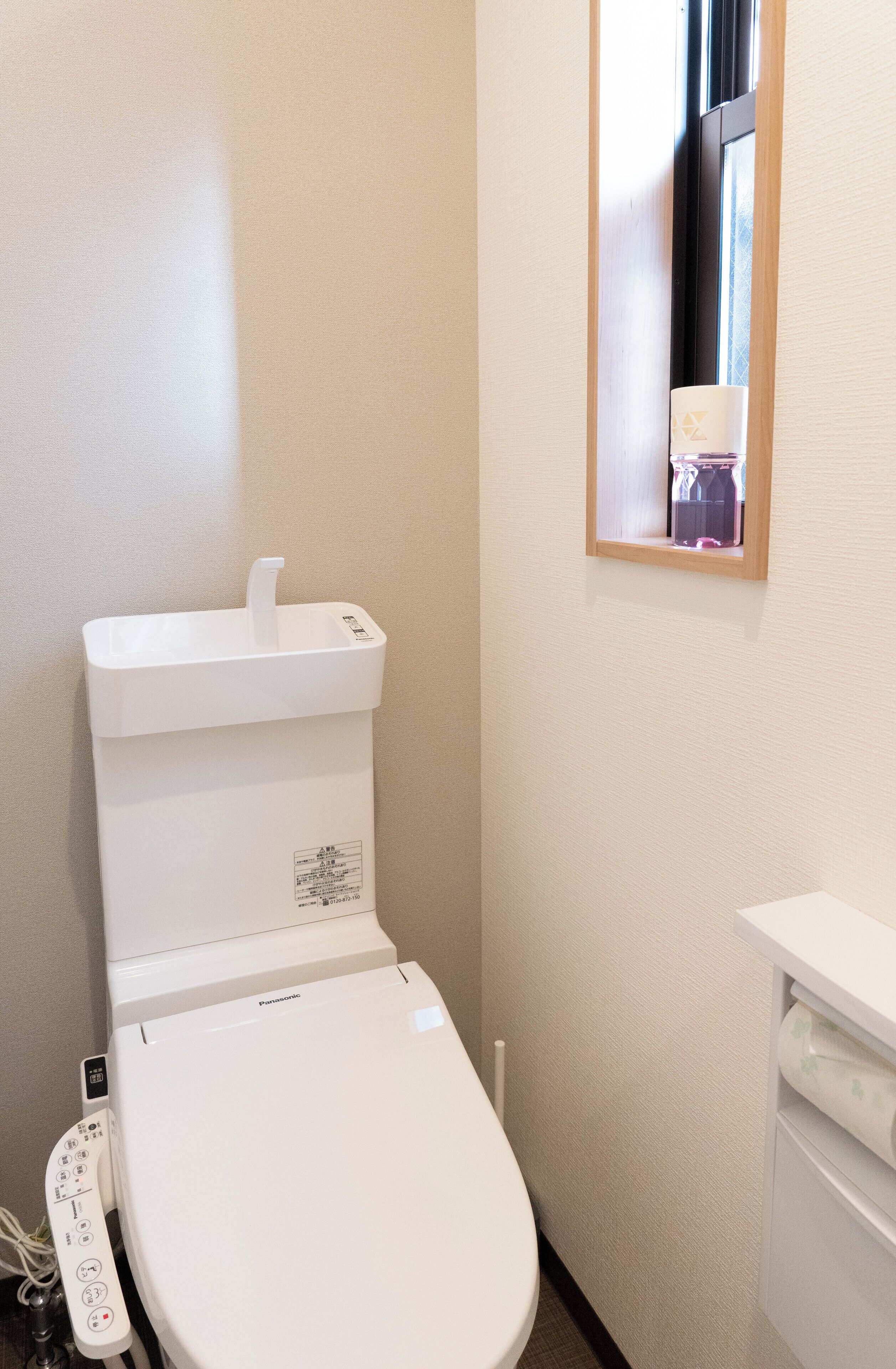A white toilet with a control panel, a small mirror, and a window with a view of a bottle.