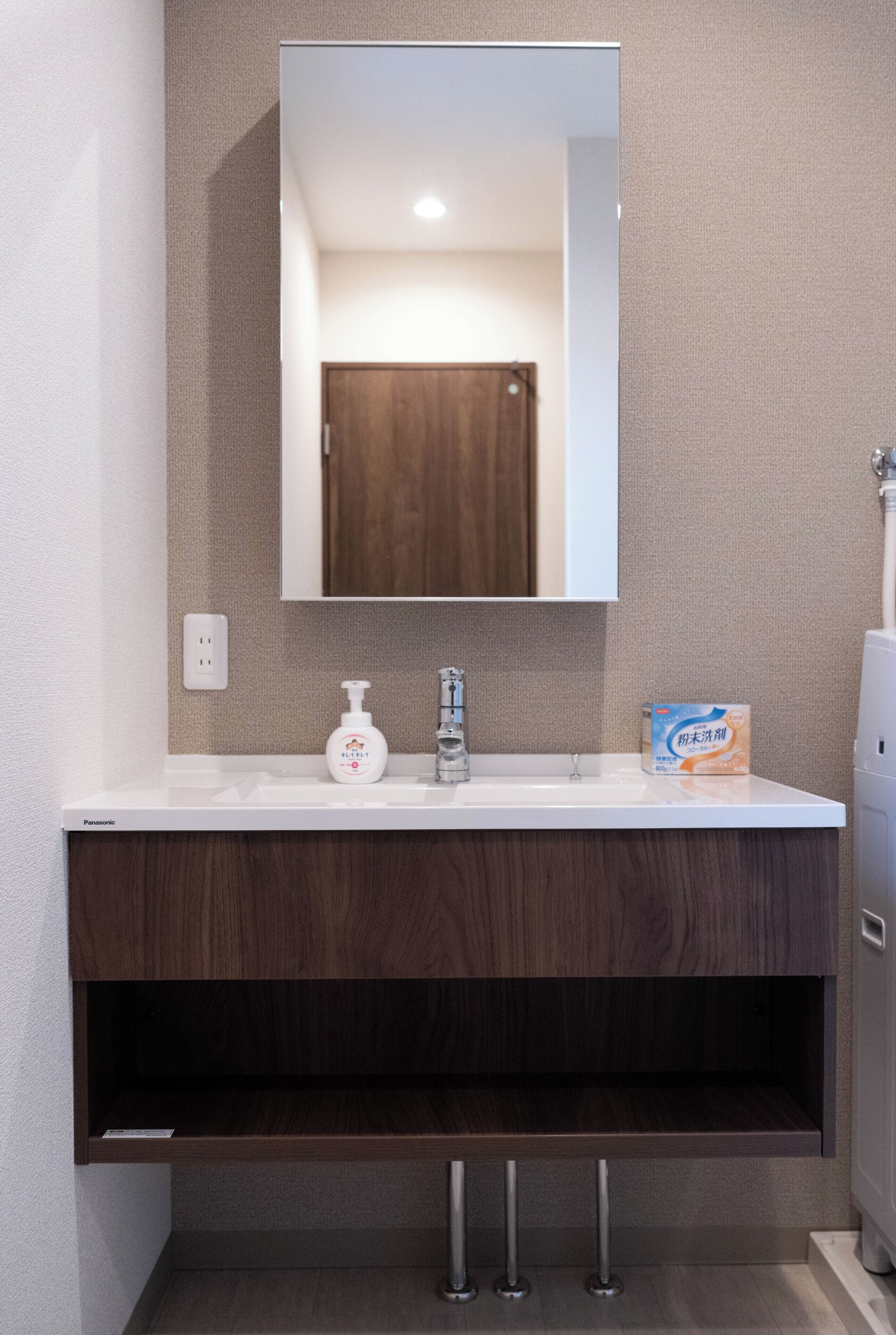 A bathroom with a white sink, a mirror, a bottle of hand soap, and a box of toilet paper.