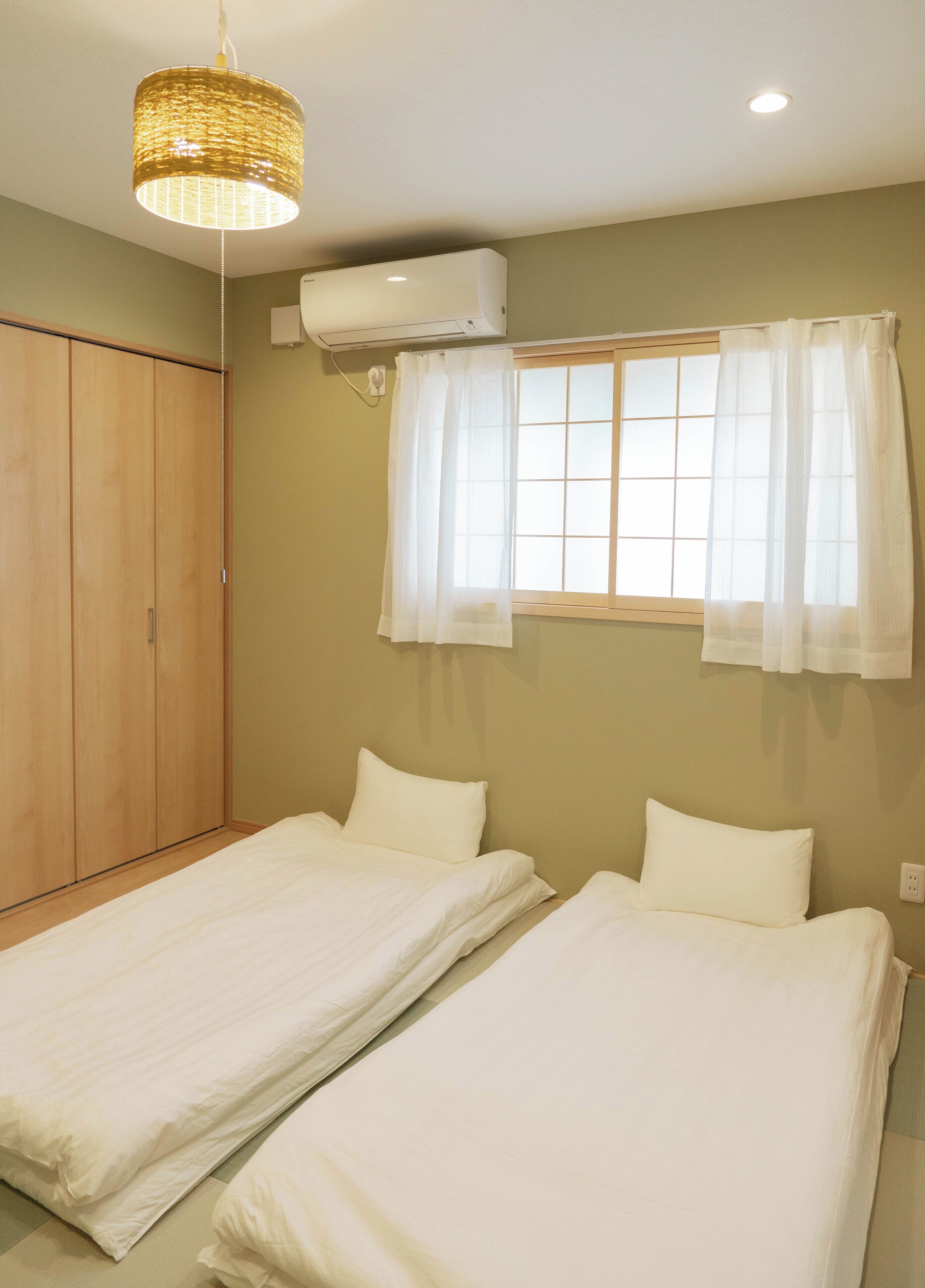 A bedroom with two beds, a wardrobe, a window with curtains, and a hanging light fixture.