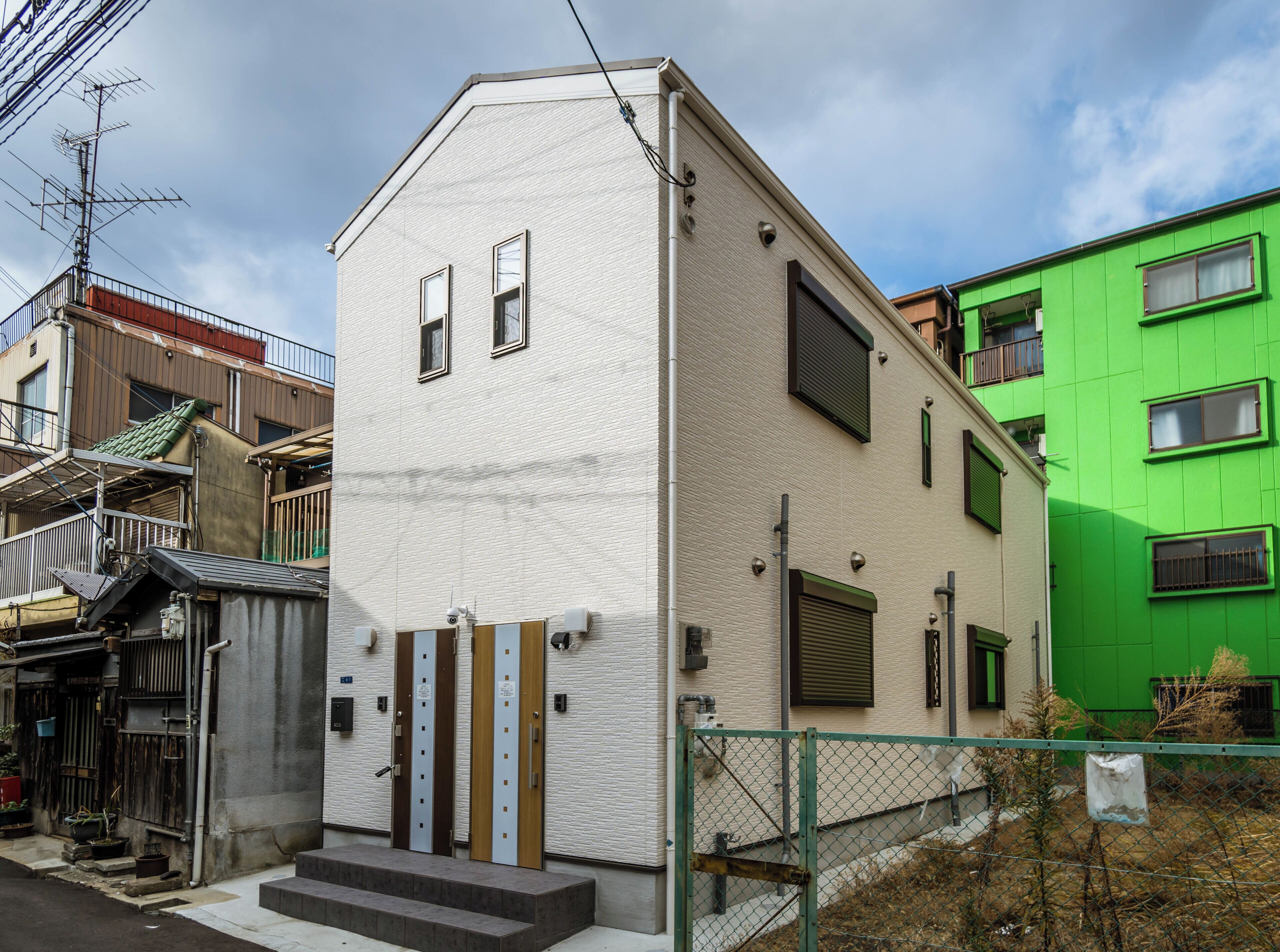 A white building with a small entrance and a green fence in front.