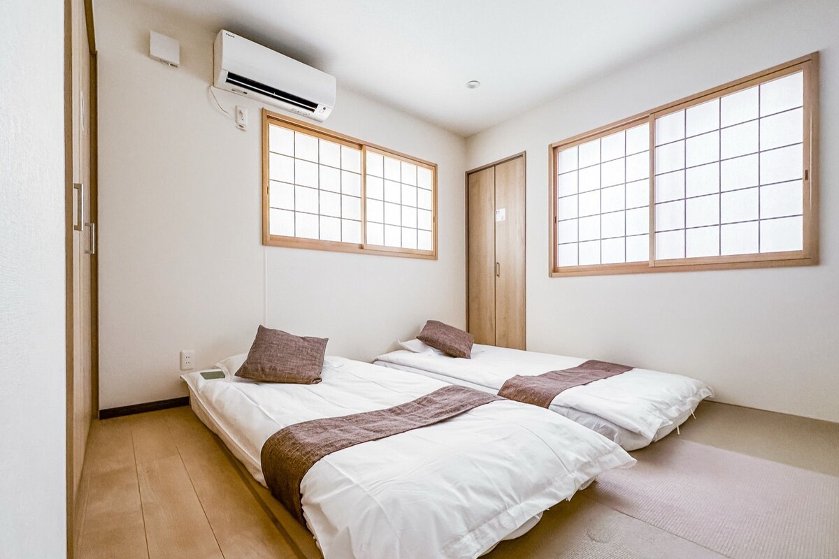 A room with two beds, a window, and an air conditioning unit.
