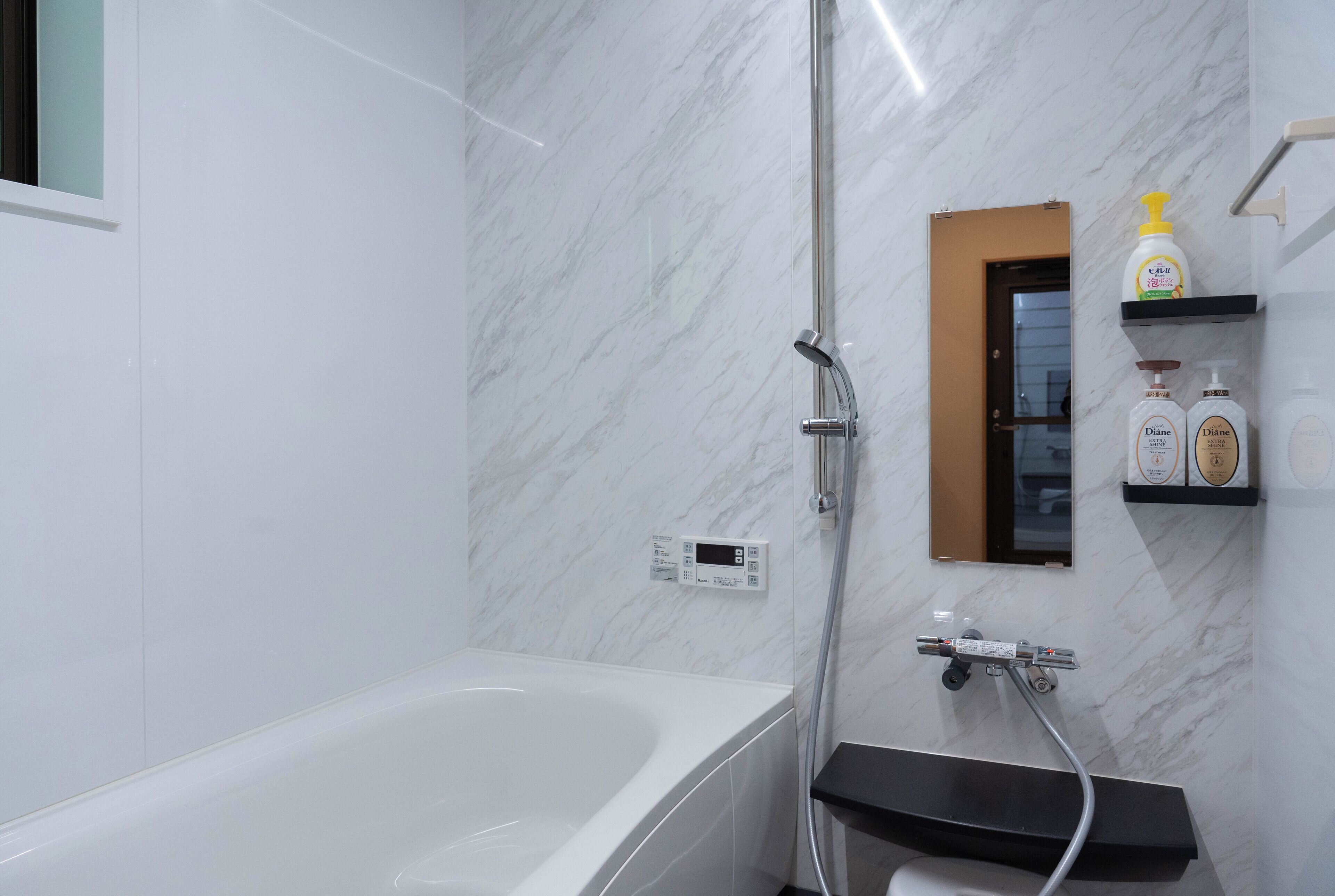 Un bagno moderno con una parete in marmo bianco, una vasca, una doccia e un piccolo ripiano con articoli da toilette.