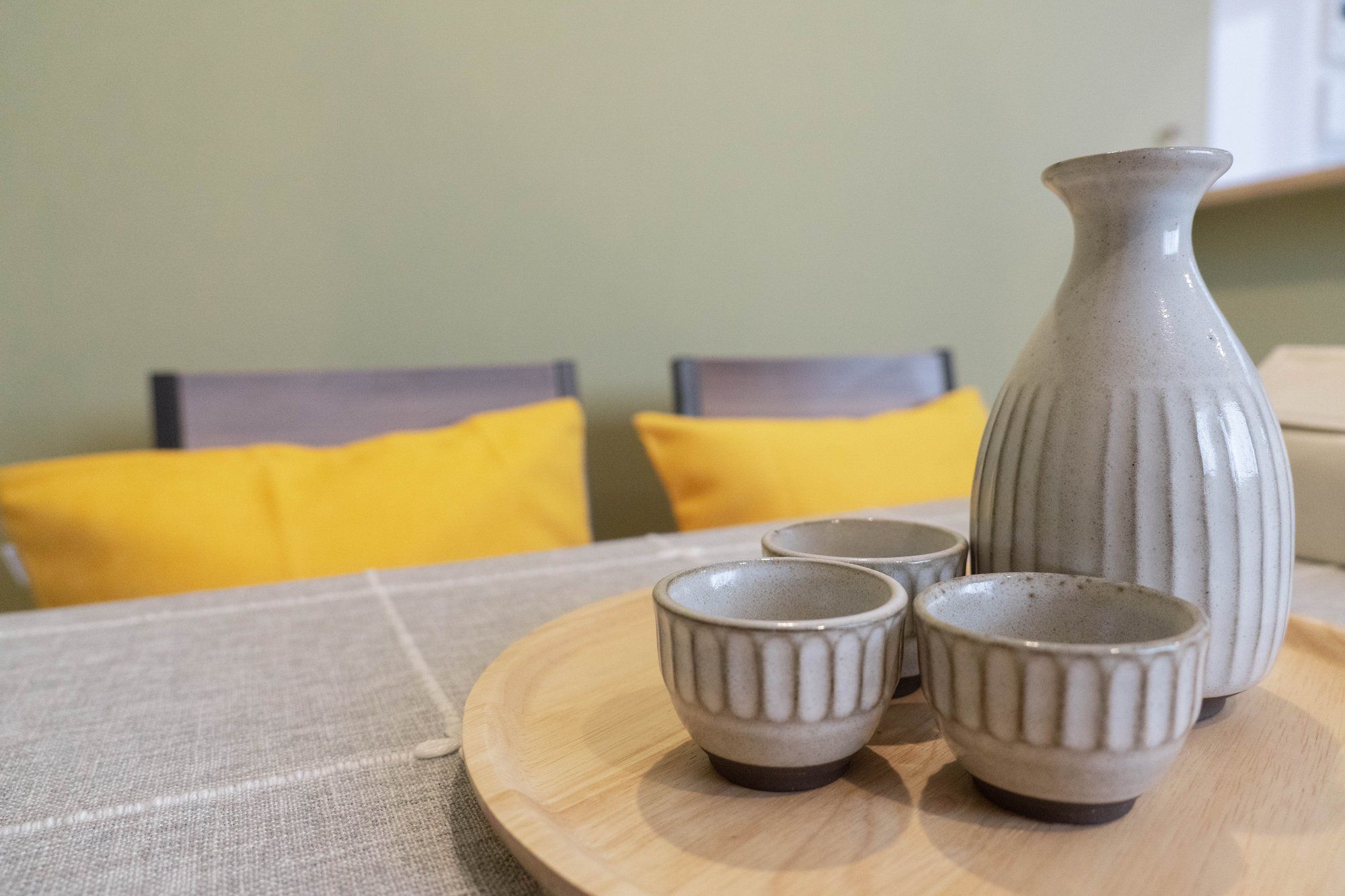 A table with a ceramic pitcher and three matching cups on a round wooden tray.