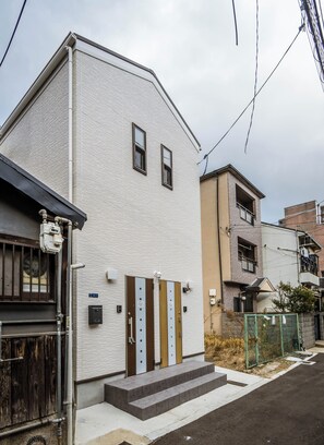 Un edificio residencial de dos plantas con fachada blanca, un juego de puertas dobles y un pequeño porche delantero.