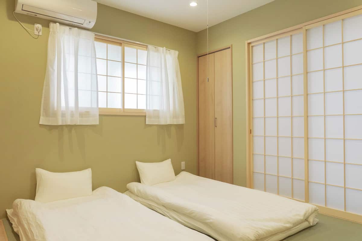 A room with two beds, a window with curtains, an air conditioning unit, and a sliding door with a grid pattern.