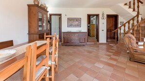 Un vaste espace de salle à manger avec une table et des chaises en bois, un buffet aux portes vitrées et un escalier menant à un autre niveau.