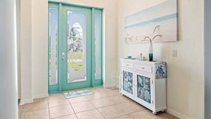 A hallway with a teal door, a white console table with decorative glass doors, and a painting on the wall.