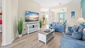 A living room with a TV, sofa, coffee table, and plants.