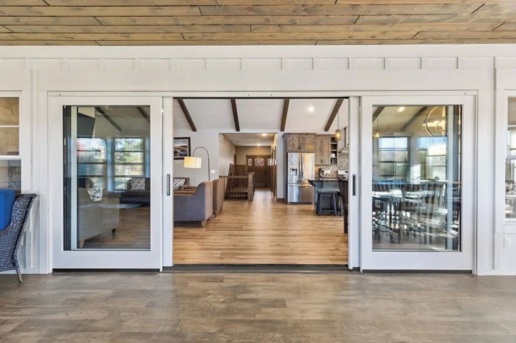 Un ambiente spazioso con pavimento in legno, una zona pranzo con sedie e tavolo, e una cucina visibile tramite porte in vetro.
