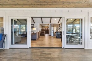 A spacious interior with a wooden floor, a dining area with chairs and a table, and a kitchen visible through glass doors.