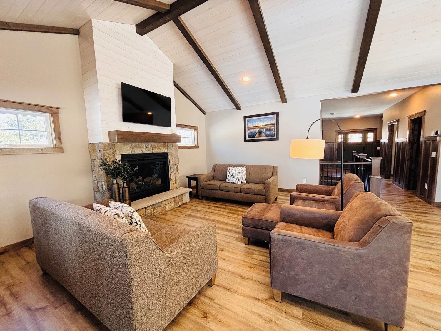 A spacious living room with a stone fireplace, a flat-screen TV mounted above it, and a large window providing natural light.