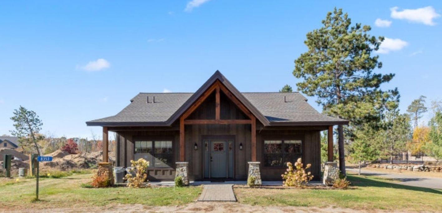 Une maison en bois à deux étages, avec un toit à pignon, un porche à l’avant et des fondations en pierre.