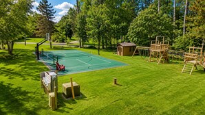 A tennis court with a wooden play structure and a small shed.