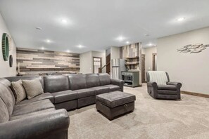 A modern living room with a sectional sofa, a small ottoman, a grey armchair, and a kitchen area in the background.