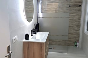 Een moderne badkamer met een houten wastafelmeubel, een witte wasbak, een spiegel en een douchehoek.