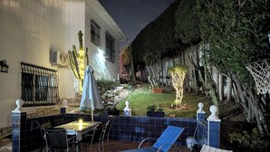 A patio with a table and chairs, a blue lounge chair, and a small garden area with plants and a tree. - 2 Bed Villa - Sleeps 5 - Private Pool & Garden (Nerja)