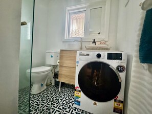 Une petite salle de bain comprenant des toilettes, un lave-linge et une petite fenêtre.