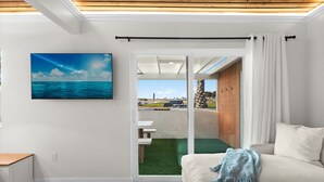 Ein modernes Wohnzimmer mit einem großen Schiebeglastür, die zu einem Außenbereich führt, einem Flachbildfernseher an der Wand und einem gemütlichen Sofa mit einer Decke.