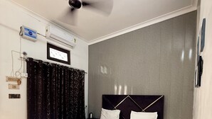 A neatly made bed with a headboard, a ceiling fan, an air conditioning unit, and a power outlet on the wall. - Saryu Sankul Homestay (Ayodhya)