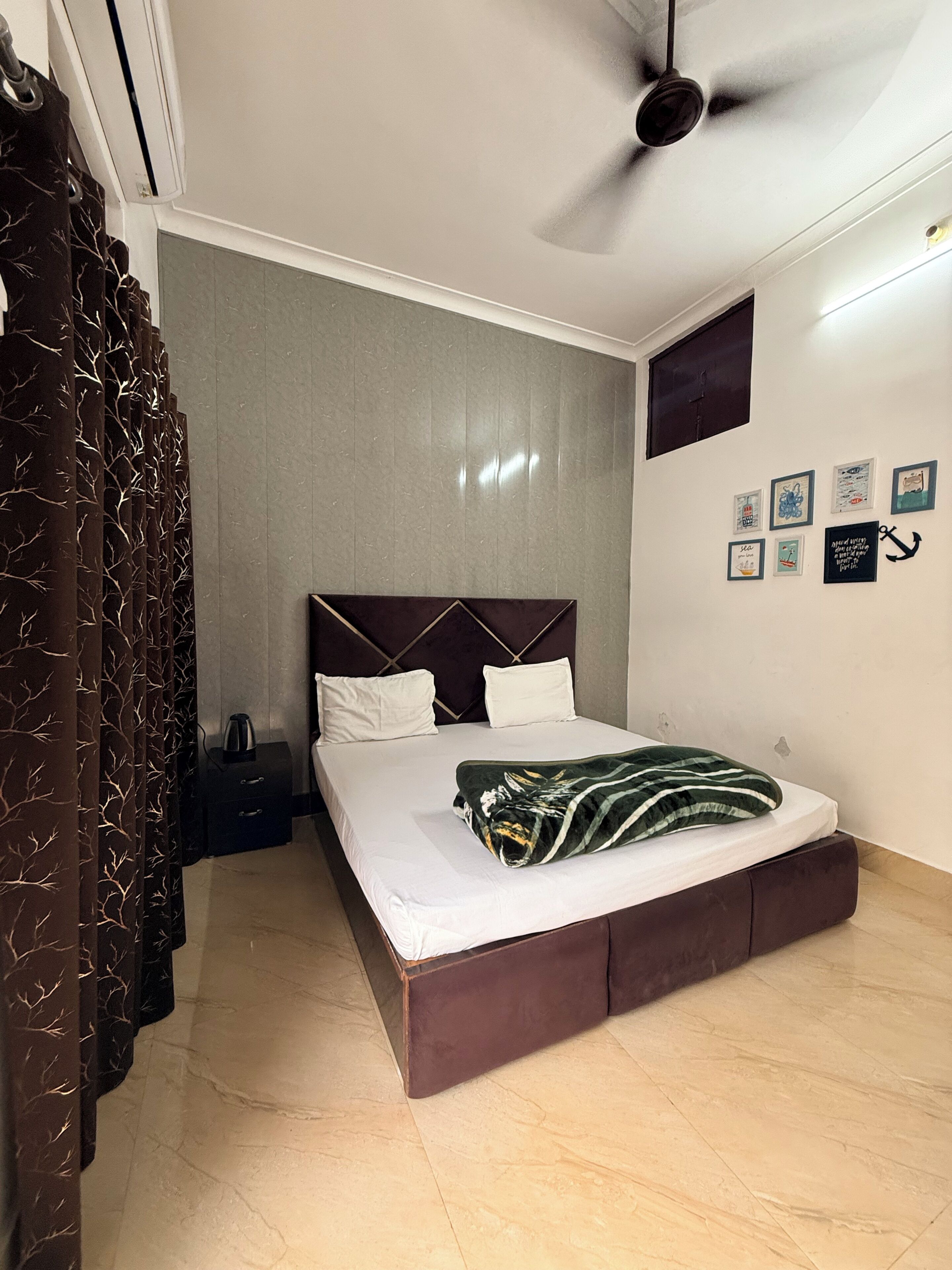 A bedroom with a bed, a ceiling fan, a nightstand, and a wall with framed pictures.