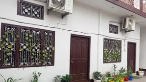 A building with multiple air conditioning units, a brown door, and a variety of potted plants. - Saryu Sankul Homestay (Ayodhya)
