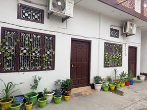 Edifici amb diverses unitats de climatització, una porta marró i una varietat de plantes en testos.
