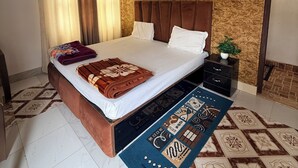 A bedroom with a bed, a ceiling fan, a TV, a nightstand, and a patterned rug. - Saryu Sankul Homestay (Ayodhya)