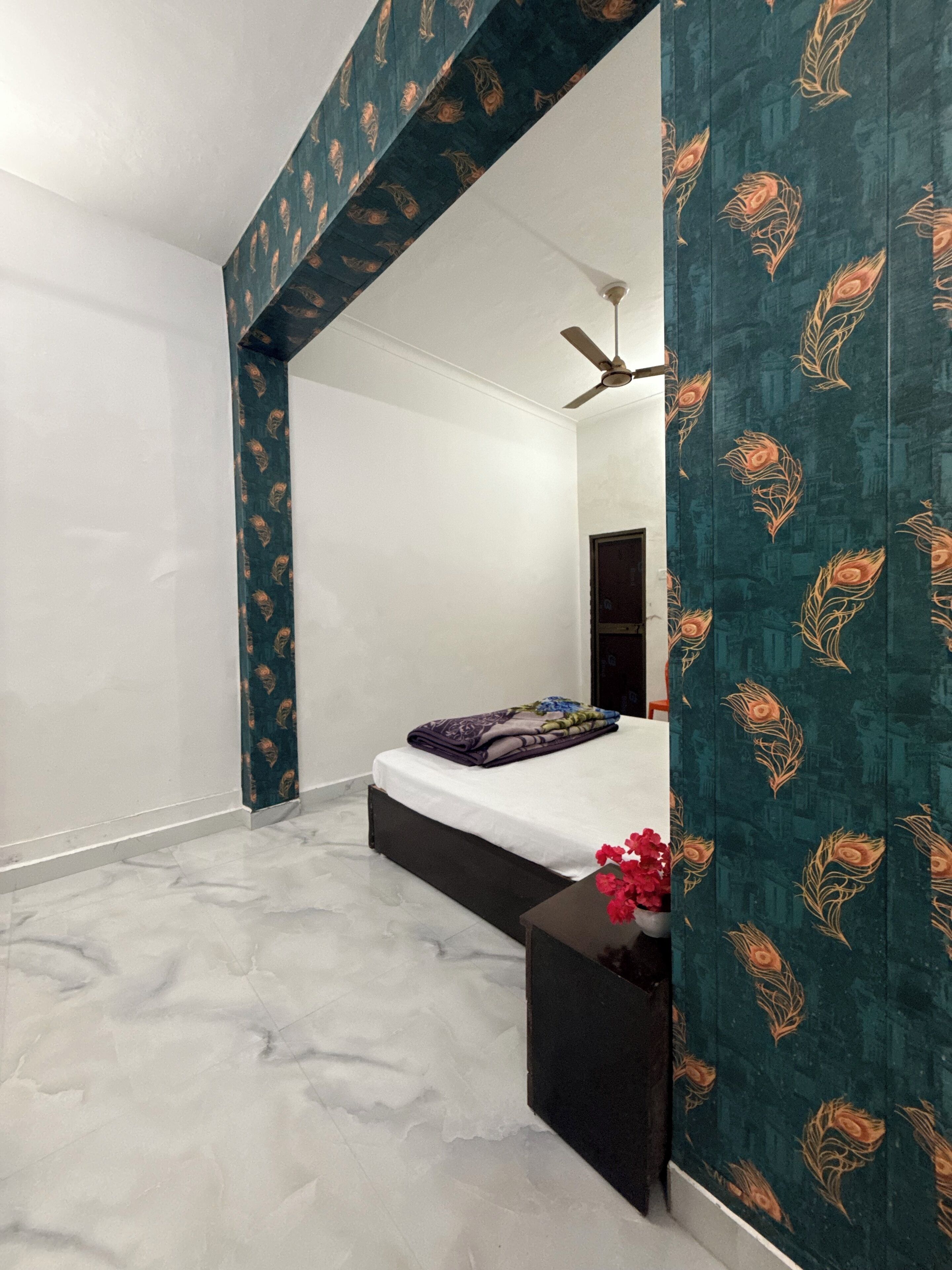 A bedroom with a bed, a ceiling fan, a nightstand, and a wall with a floral pattern.
