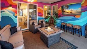 A room with a colorful mural, a fire pit, wicker furniture, and a view of the outside.