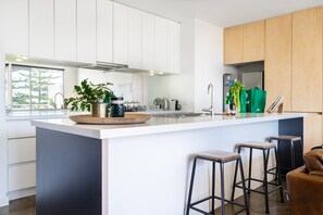 A modern kitchen with white cabinets, a large island with stools, and a stainless steel refrigerator.