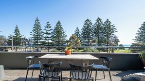 An outdoor seating area with a table and chairs, a potted plant, and a view of trees and the sea. - Aquabelle One on Rye Beach (Rye)