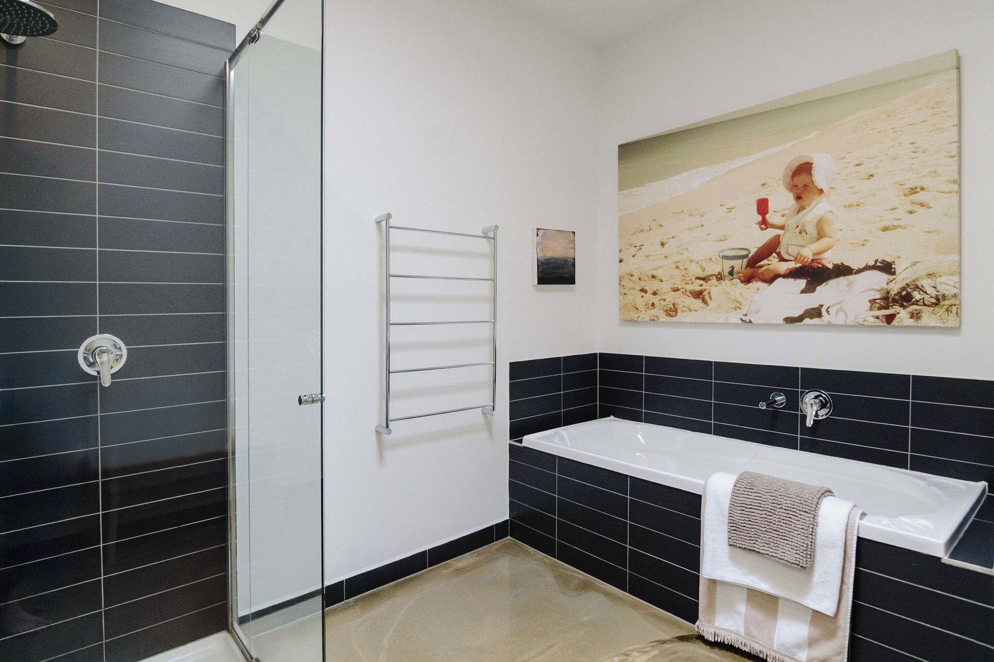 Ein modernes Badezimmer mit einer Glasdusche, einer weißen Badewanne und einer Wand mit schwarzen Fliesen.