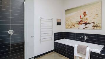 Ein modernes Badezimmer mit einer Glasdusche, einer weißen Badewanne und einer Wand mit schwarzen Fliesen.