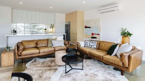 A modern living room with two brown leather sofas, a round coffee table, and a fur rug. There is a kitchen area with white cabinets and a refrigerator. - Aquabelle One on Rye Beach (Rye)