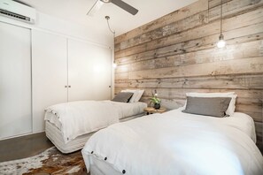 A bedroom with two beds, a ceiling fan, and a wooden wall. - Aquabelle One on Rye Beach (Rye)