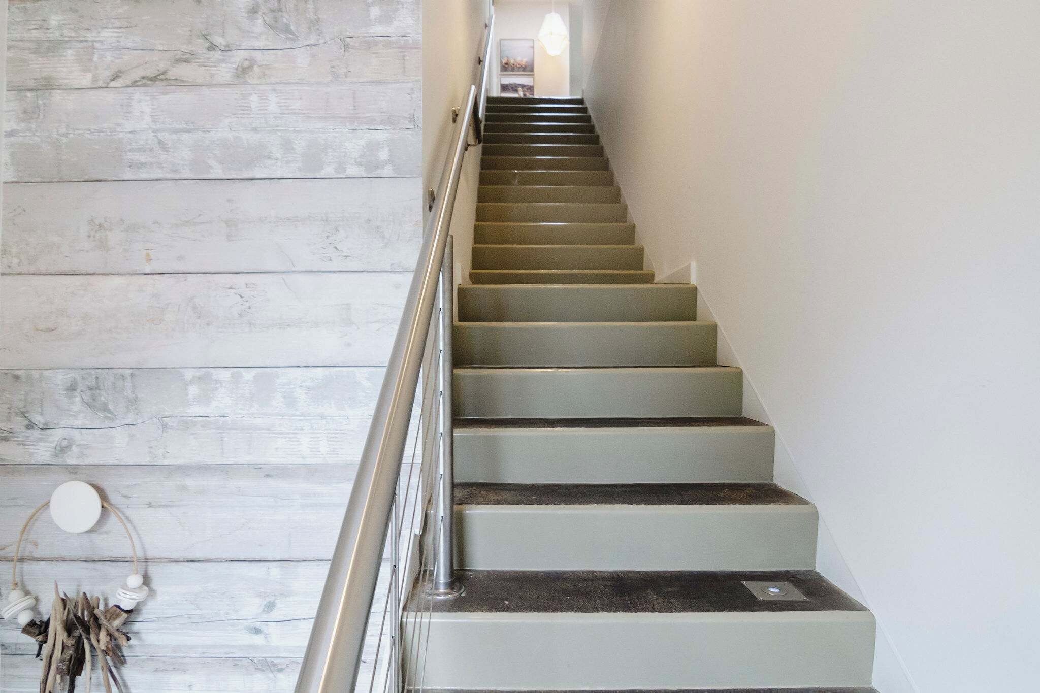 A staircase with a metal handrail, wooden wall paneling, and a hanging dreamcatcher.