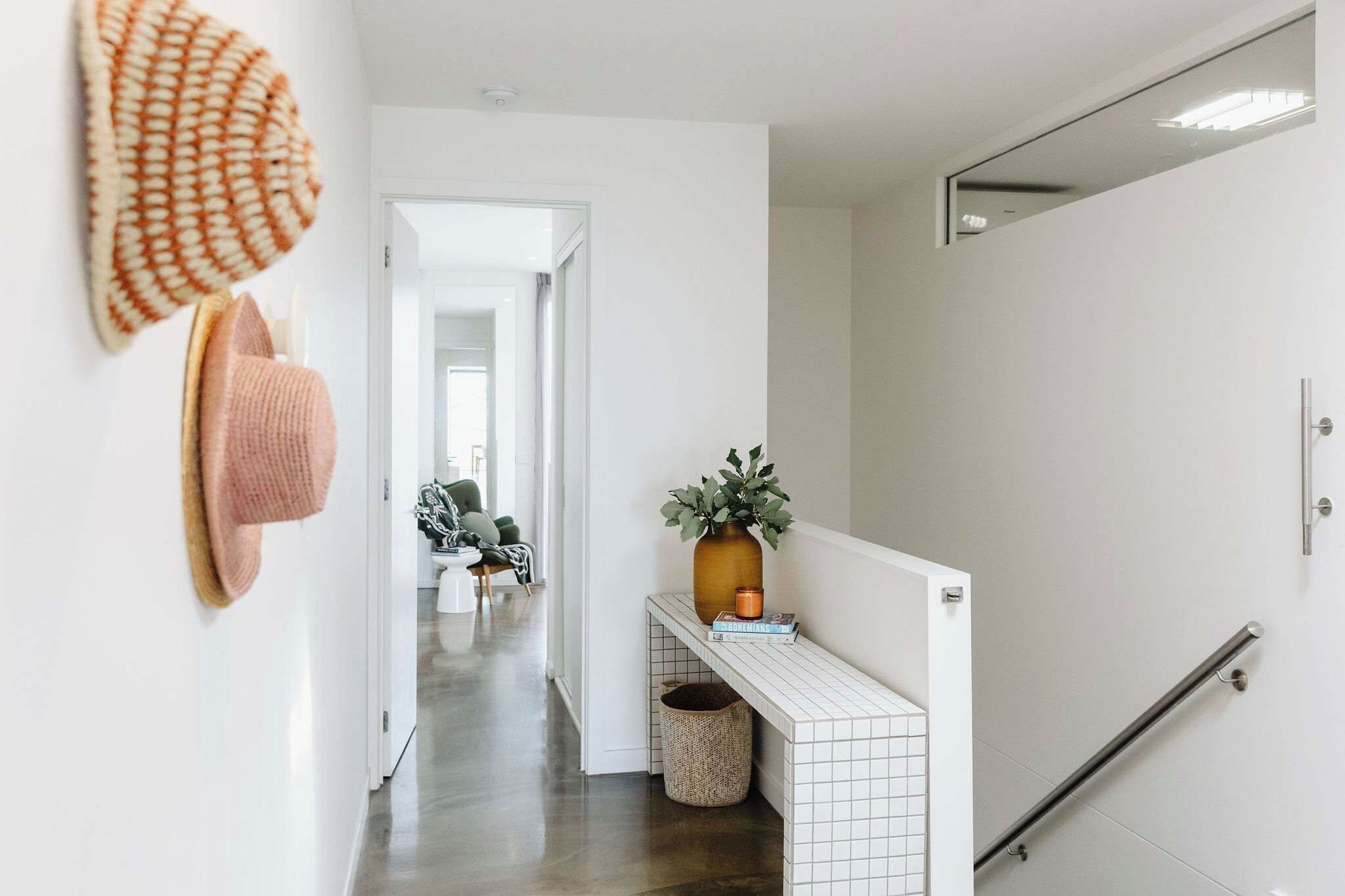 A hallway with a white tiled wall, a small plant on a shelf, and a handrail on the right.