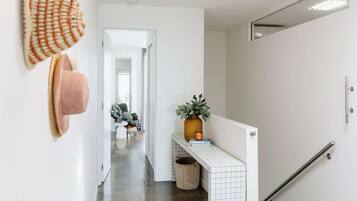 A hallway with a white tiled wall, a small plant on a shelf, and a handrail on the right.