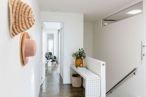 Un couloir avec un mur recouvert de carreaux blancs, une petite plante posée sur une étagère et une main courante sur le côté droit.