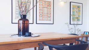A wooden dining table with a vase of branches, framed menus on the wall, and black chairs. - Aquabelle Four on Rye Beach (Rye)