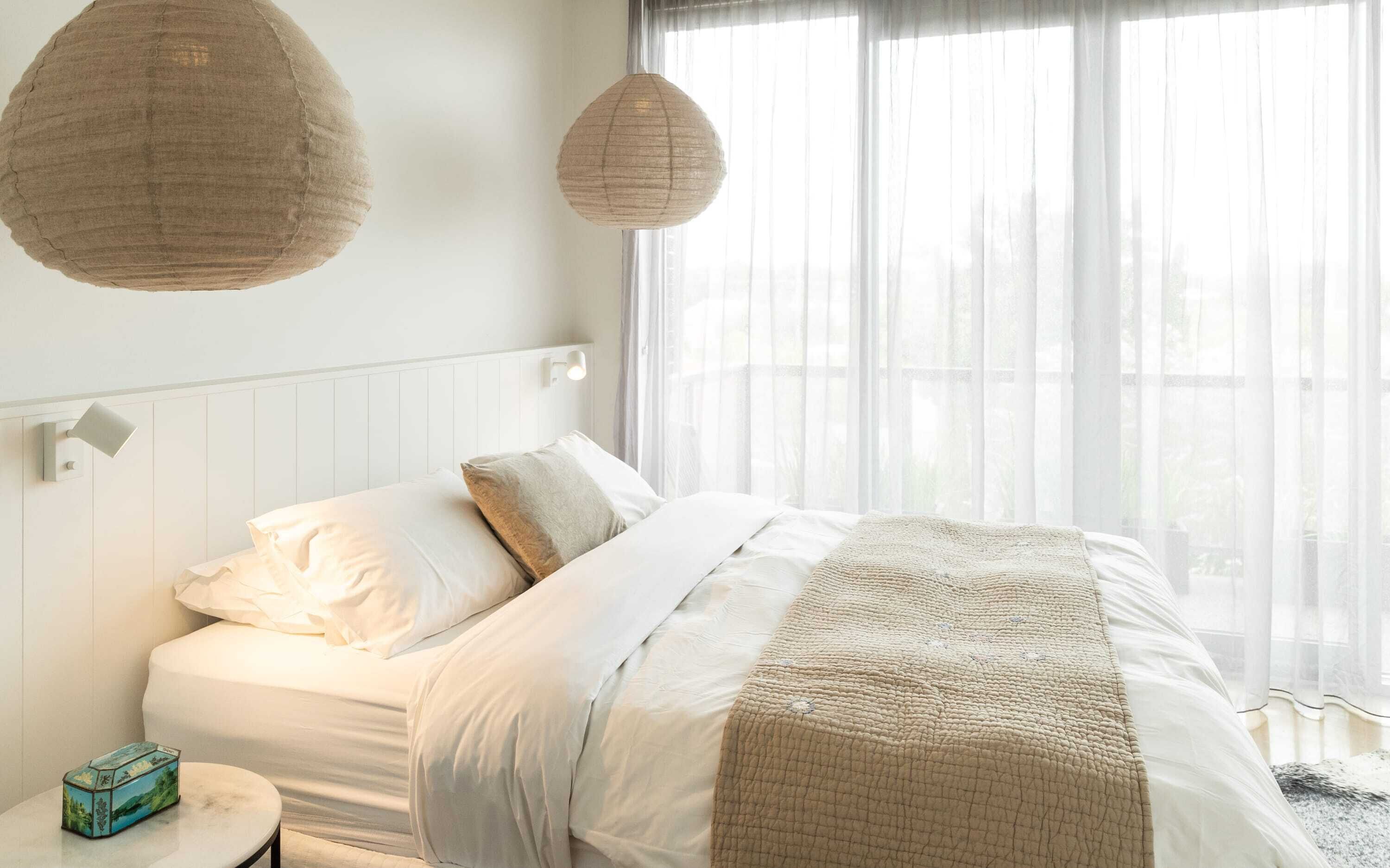 Ein Schlafzimmer mit einem Bett, Nachttischen und einem Fenster mit durchsichtigen Vorhängen.