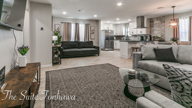 Una sala de estar moderna con un sof á, una mesa de centro y una alfombra. Hay una zona de cocina con un refrigerador y una mesa de comedor.